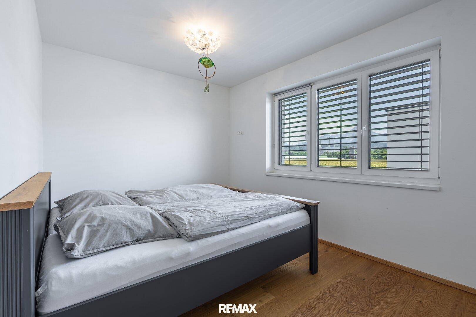 Helles Schlafzimmer mit Doppelbett, Holzboden und großen Fenstern.
