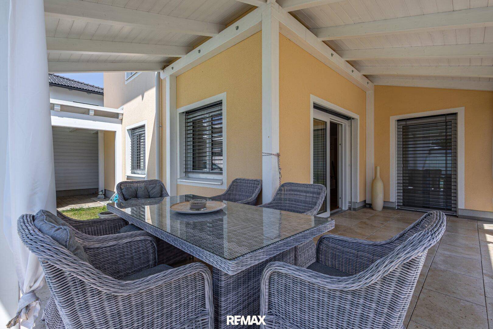 Gemütlicher überdachter Terrassenbereich mit Rattan-Sitzgruppe und Blick in den Garten.
