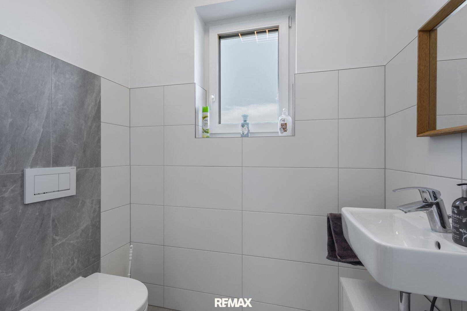 Modernes Gäste-WC mit wandhängendem WC, Waschbecken und Fenster.