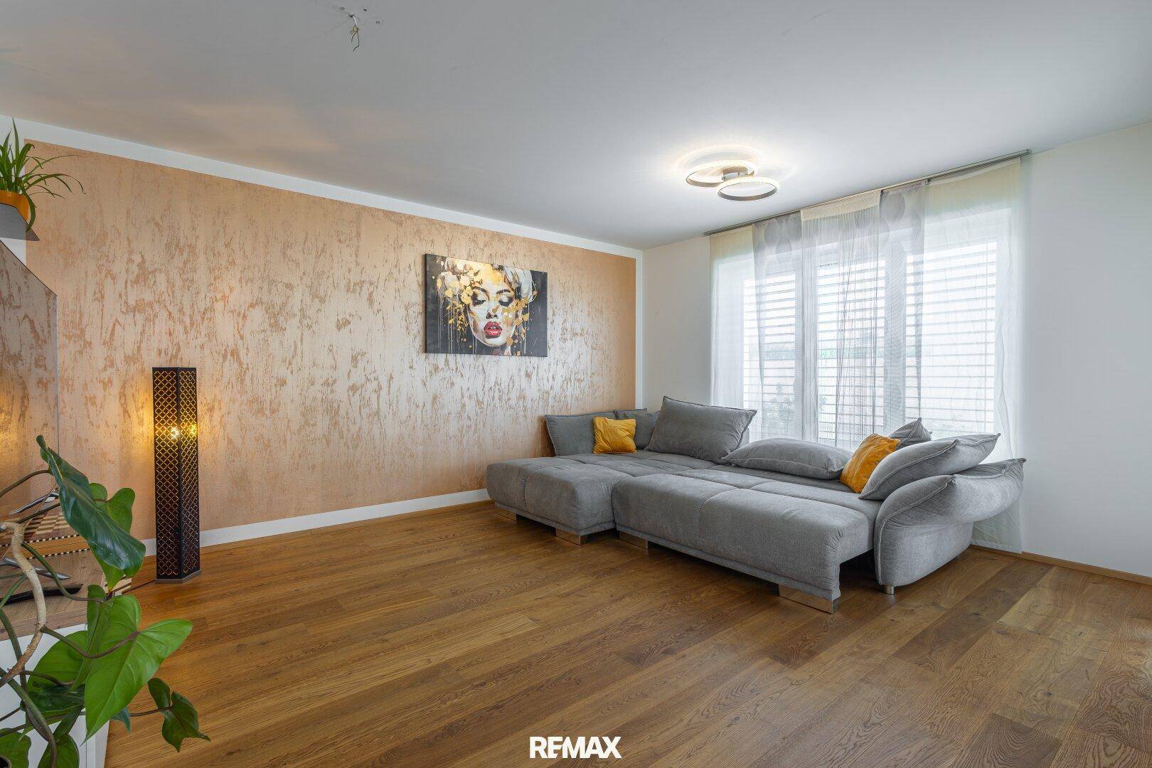 Helles Wohnzimmer mit bequemer Couch, Holzboden und großen Fenstern.