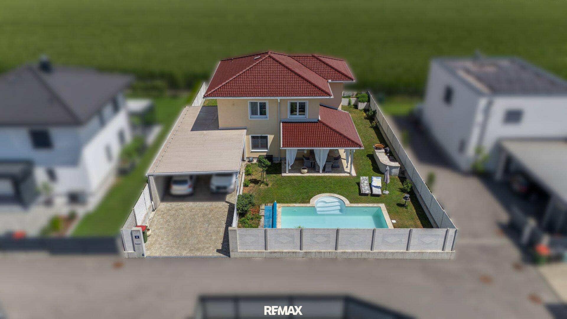 Gesamtansicht des Hauses aus der Luft mit Pool, Carport und umliegender Bebauung.