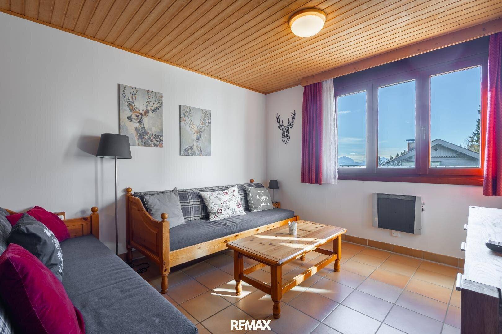 Heller Wohnbereich mit Holzdecke, bequemen Sofas und Blick auf die Berge durch große Fenster.