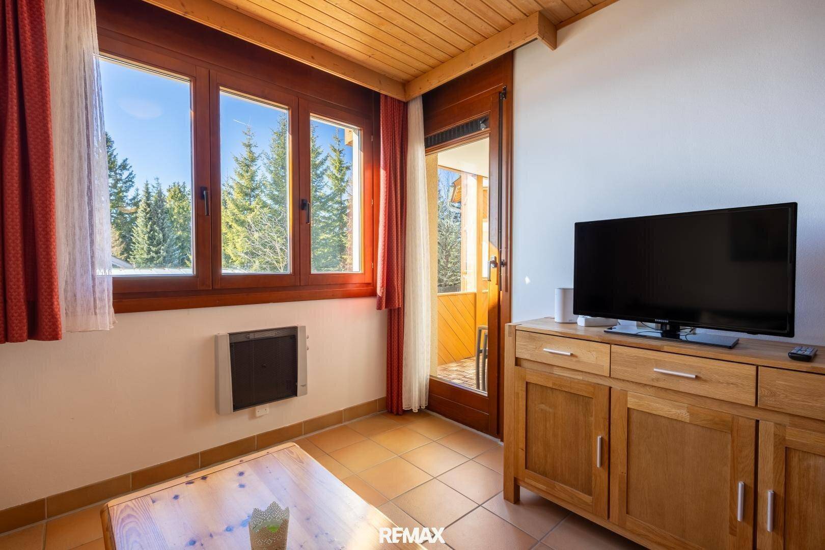 Heller Wohnbereich mit Zugang zum Balkon, Fliesenboden und Blick auf verschneite Bäume.