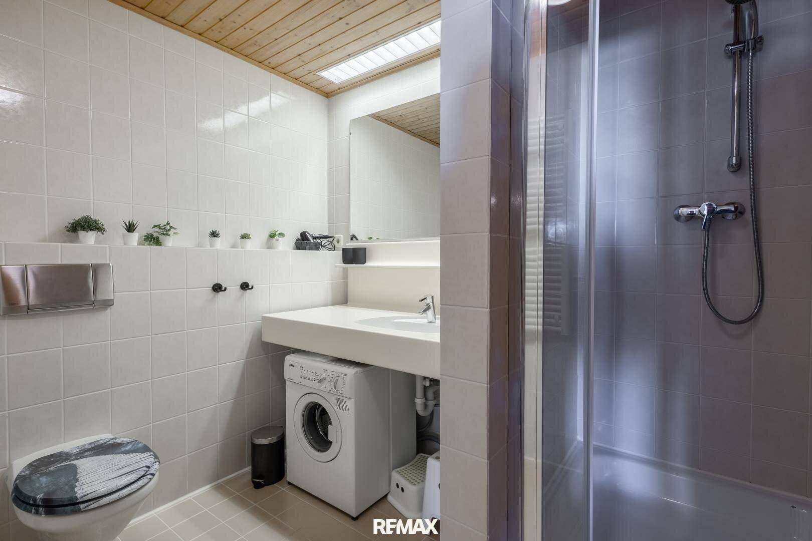 Modernes Badezimmer mit Dusche, Waschbecken und integrierter Waschmaschine unter dem Waschtisch.