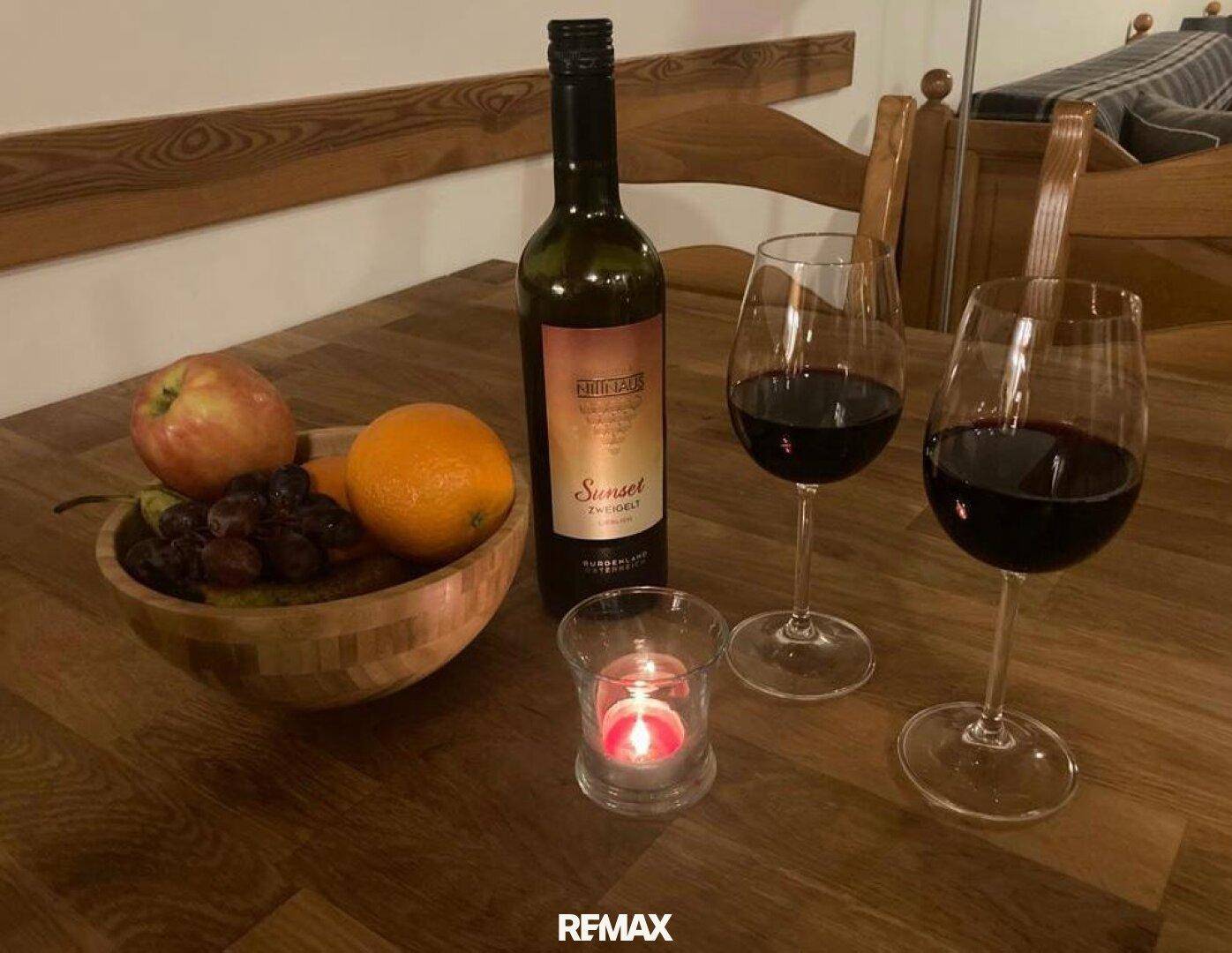 Nahaufnahme eines gedeckten Tisches mit Wein, Gläsern und Obstschale in gemütlicher Atmosphäre.