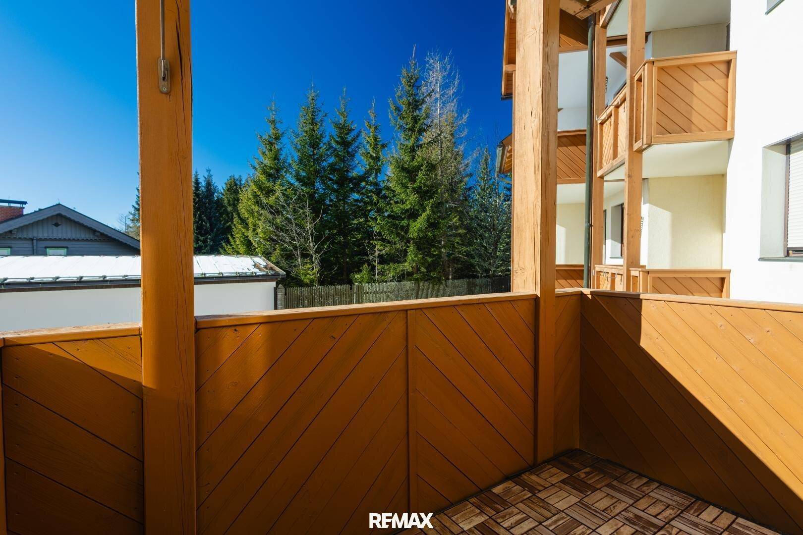 Leerer Holzbalkon mit Blick auf Bäume und andere Gebäude, bereit zur Möblierung.