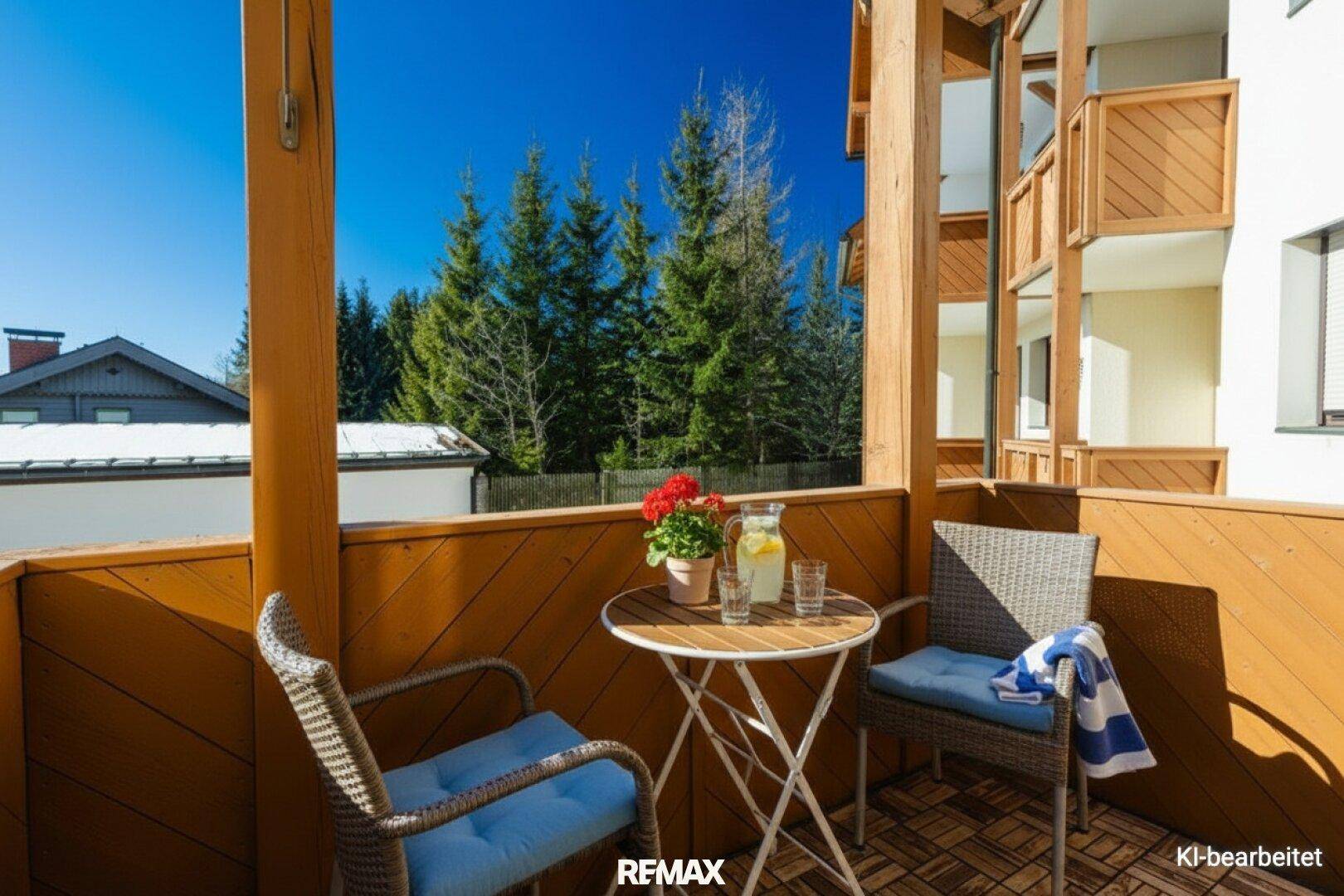 Gemütlicher Holzbalkon mit Sitzgelegenheiten, Blumen und Blick auf die umliegenden Bäume.