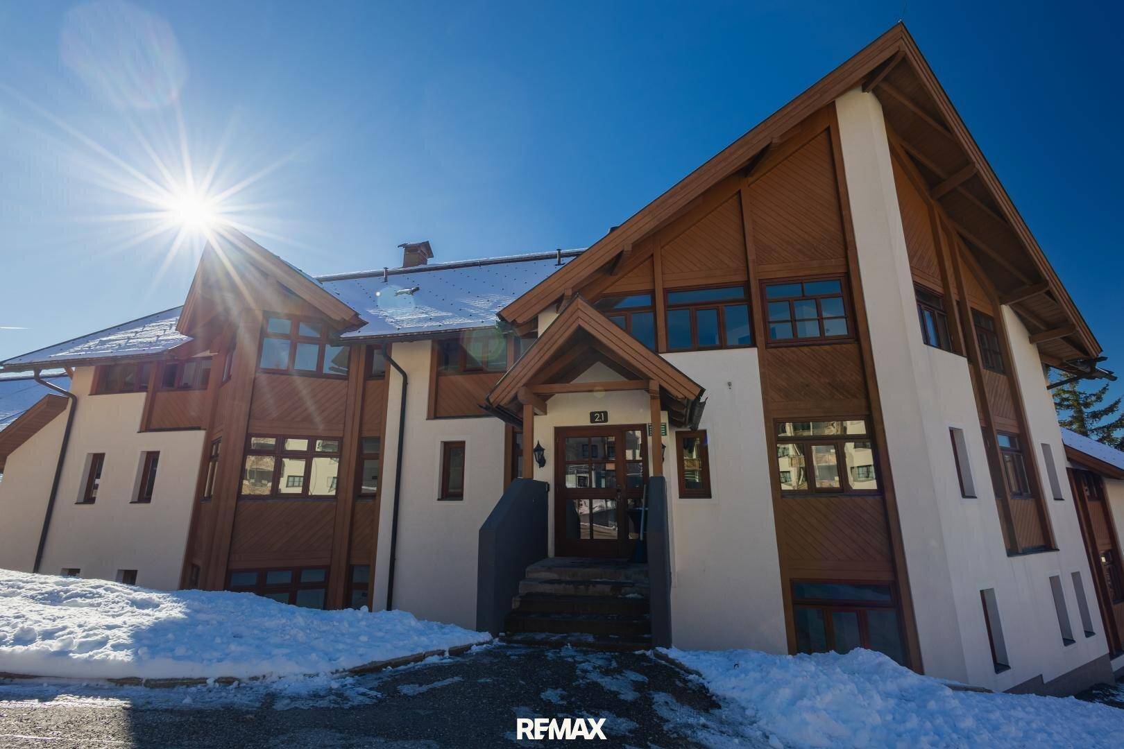 Attraktives Mehrfamilienhaus im alpinen Stil mit Holzfassade und verschneiter Umgebung.
