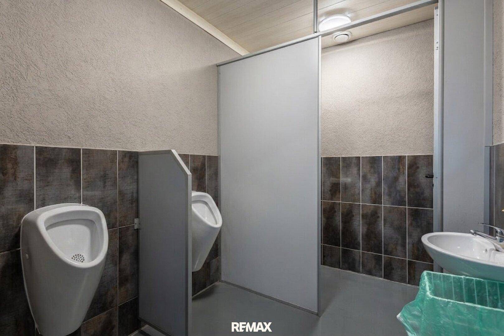 Funktionaler Herrenwaschraum mit Urinalen, Trennwänden und dunklen Fliesen an den Wänden und auf dem Boden.