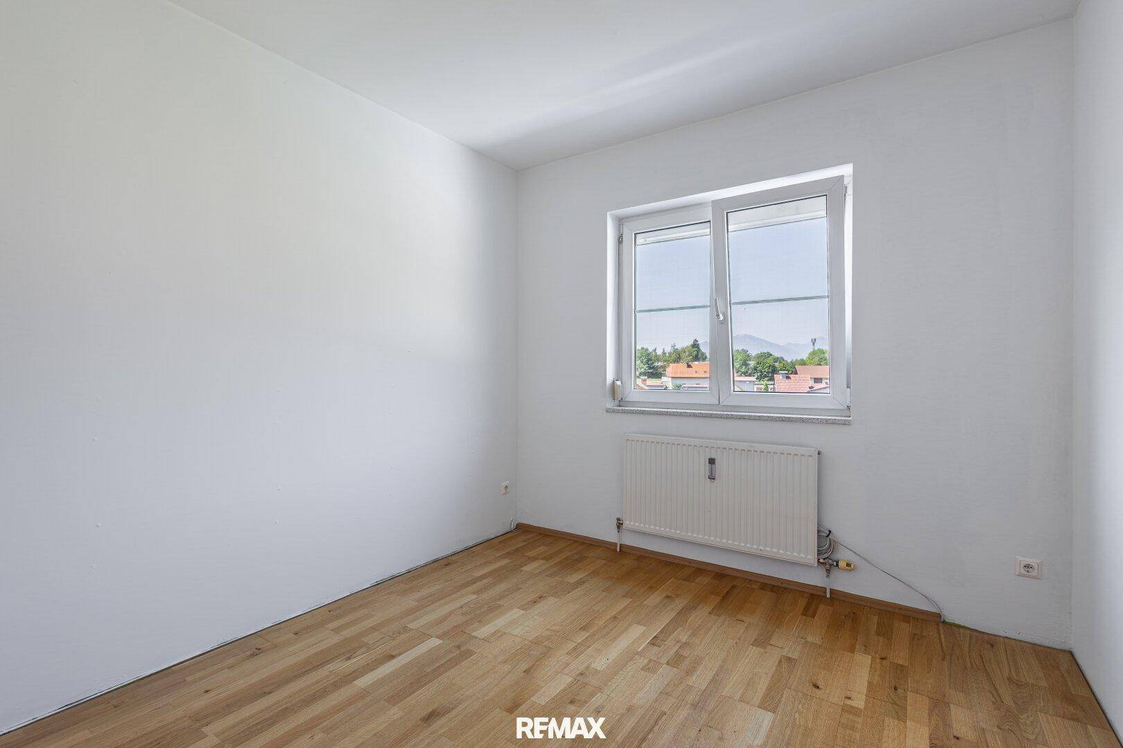 Unmöbliertes Zimmer mit Parkettboden und großem Fenster, ideal für ein Kinderzimmer oder Büro.