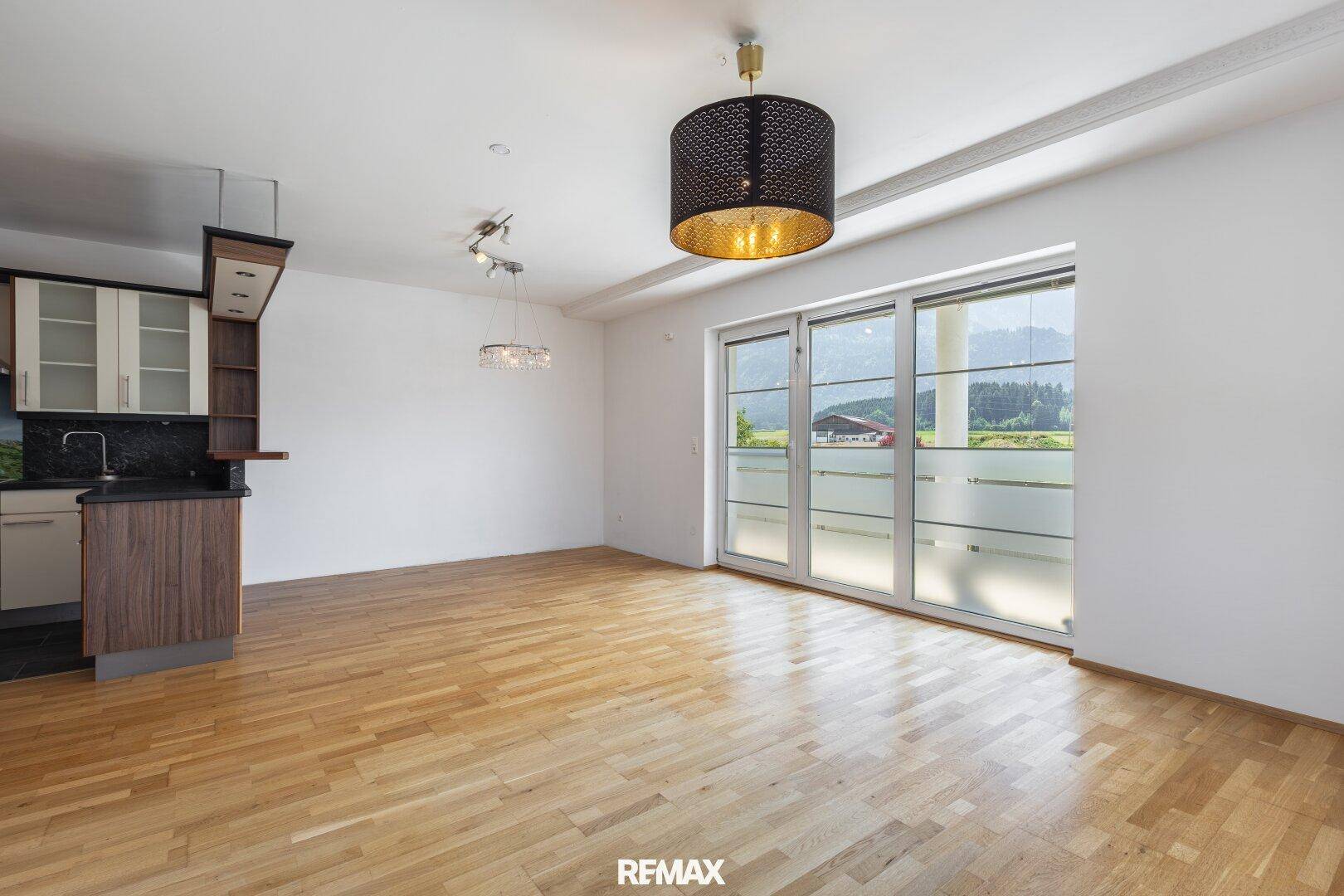 Geräumiger Wohnbereich mit Zugang zum Balkon und Blick auf die umliegende Landschaft und Berge.