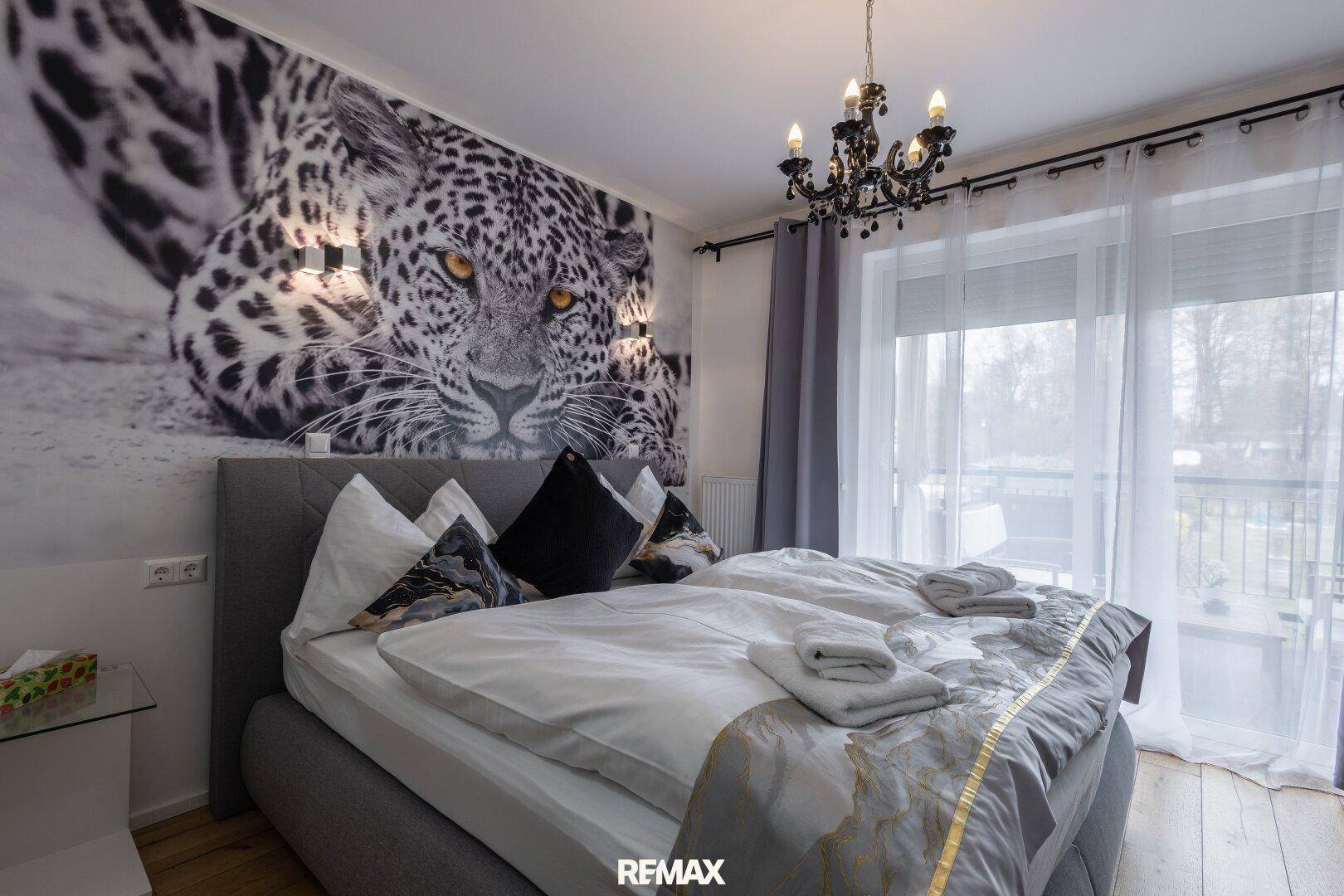 Schlafzimmer mit großem Bett, auffälligem Leoparden-Wandbild und Zugang zum Balkon.