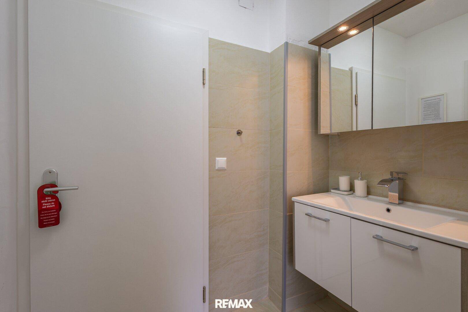 Modernes Badezimmer mit Waschtisch, Spiegelschrank und begehbarer Dusche in hellen Fliesen.