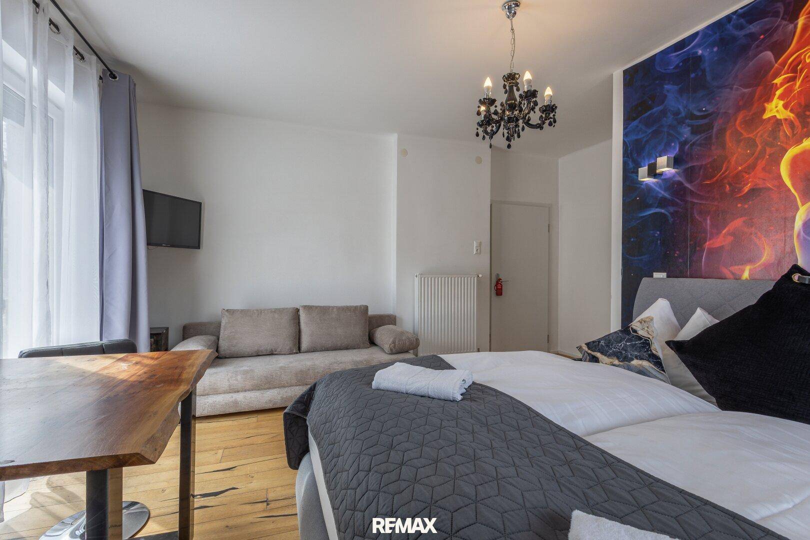 Schlafzimmer mit Doppelbett, Sofa, kleinem Tisch und farbenfroher Wanddekoration.