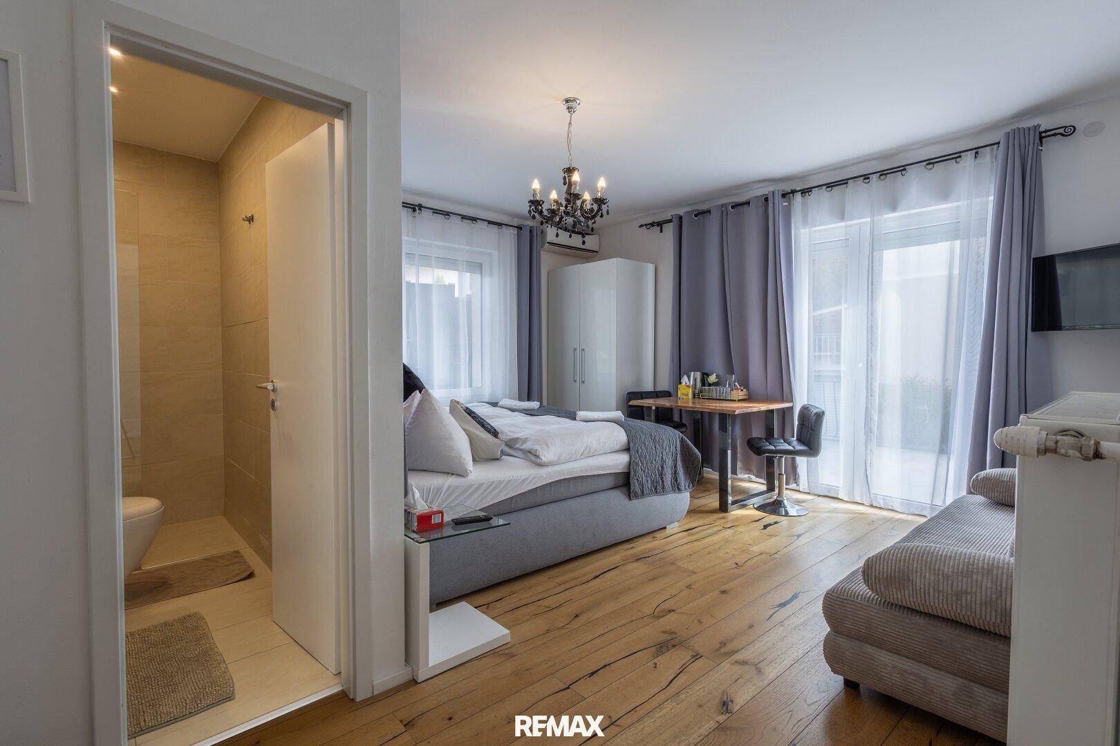 Helles Schlafzimmer mit Holzboden, Kleiderschrank und offenem Zugang zum Badezimmer.