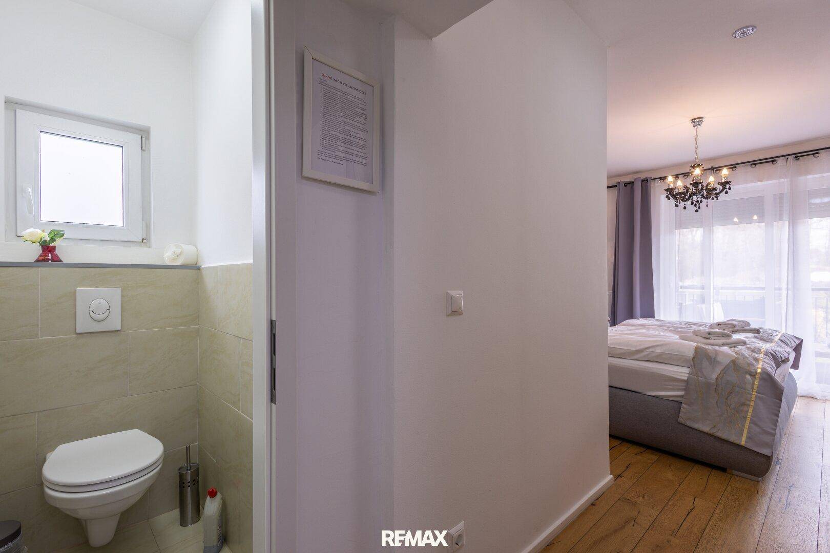 Separater Toilettenbereich mit Fenster und Wand-WC, angrenzend an ein Schlafzimmer.