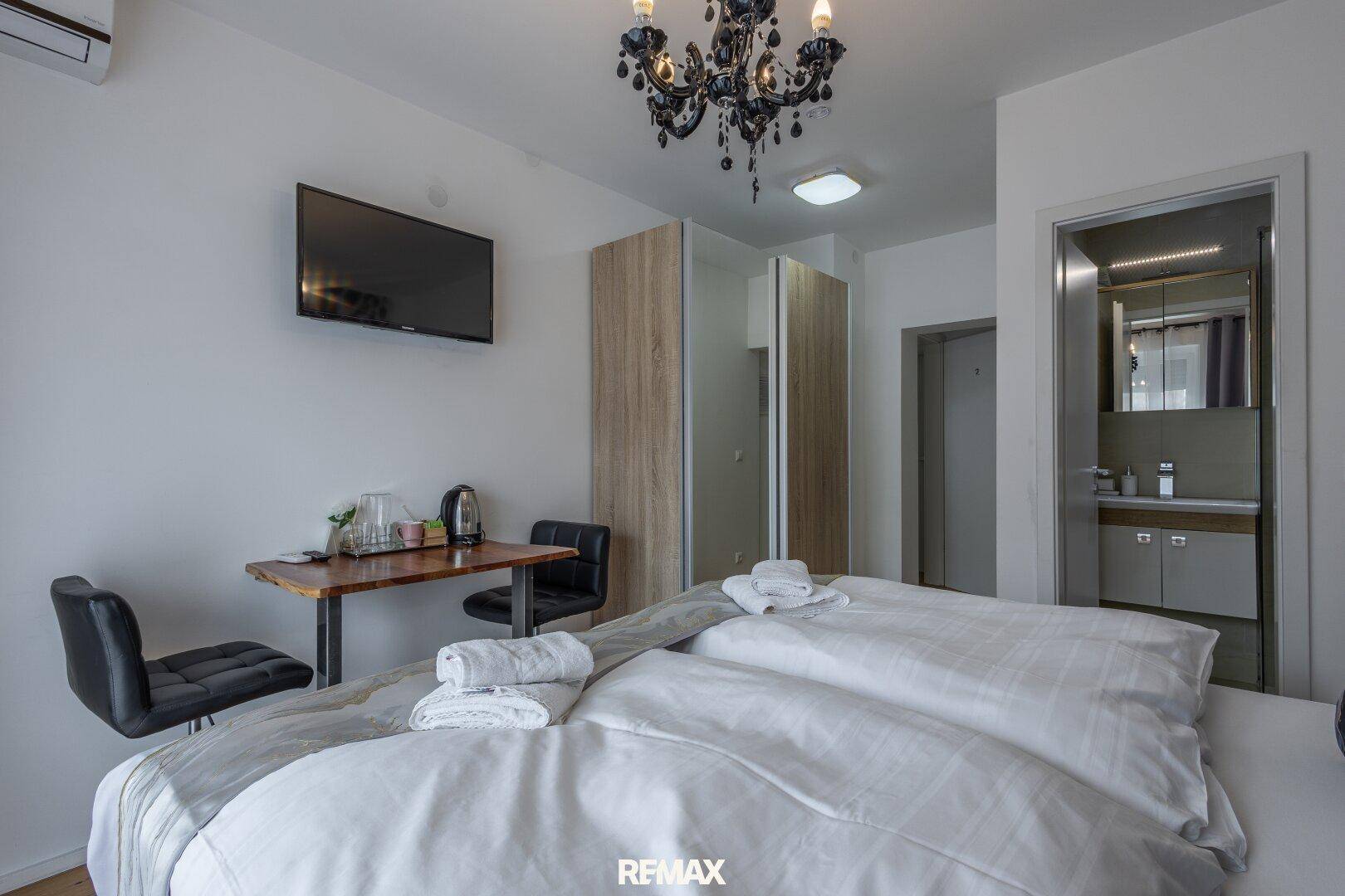 Schlafzimmer mit Doppelbett, kleinem Schreibtisch und offenem Zugang zum Badezimmer.