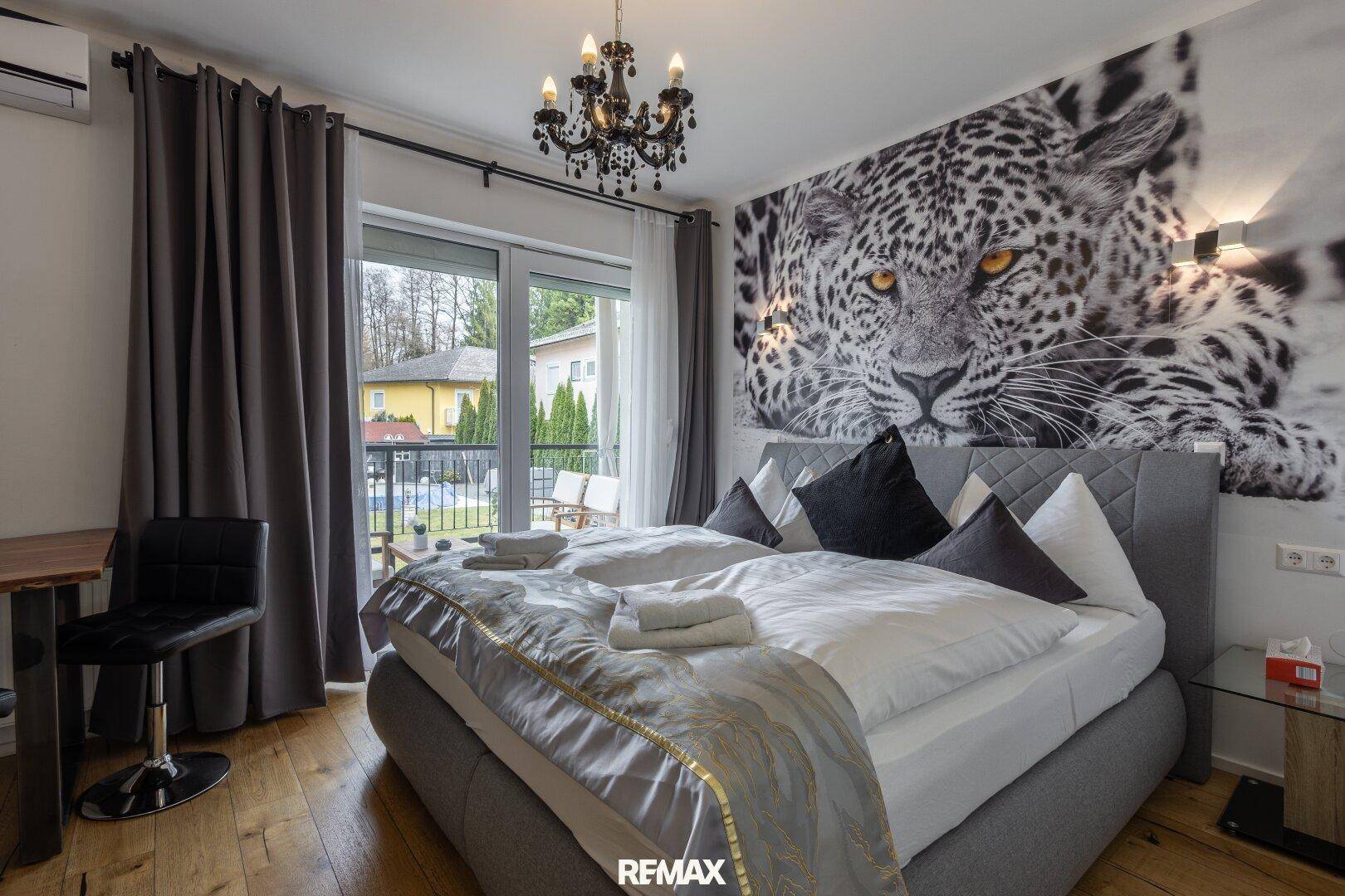 Geräumiges Schlafzimmer mit großem Bett, Leoparden-Wandbild und Balkonzugang.