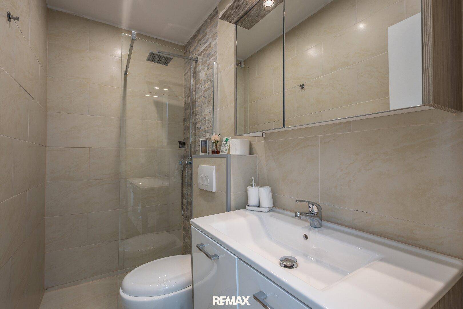 Modernes Badezimmer mit Waschtisch, Spiegelschrank, WC und begehbarer Regendusche.