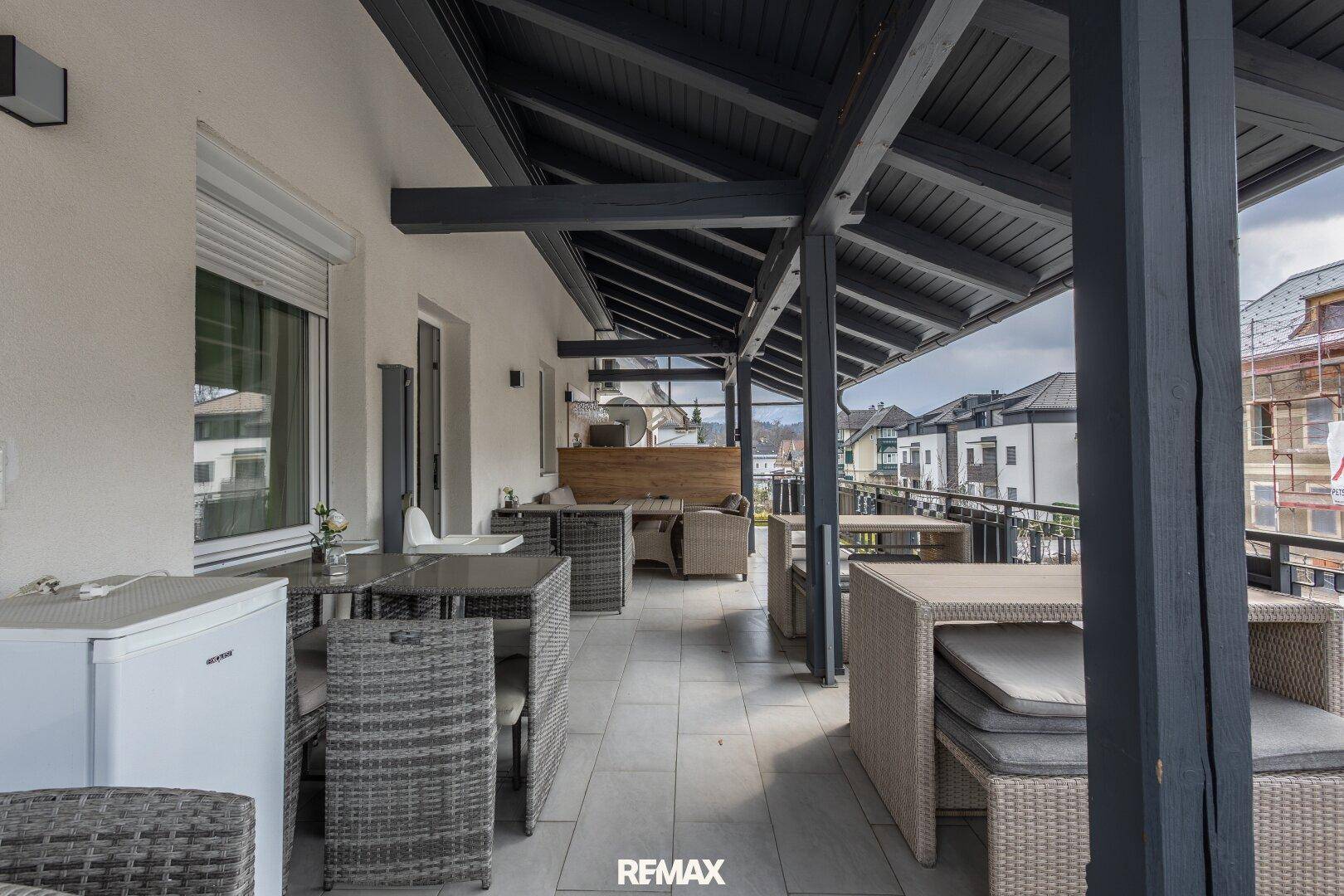 Große überdachte Terrasse mit zahlreichen Outdoor-Sitzgelegenheiten und Tischen.