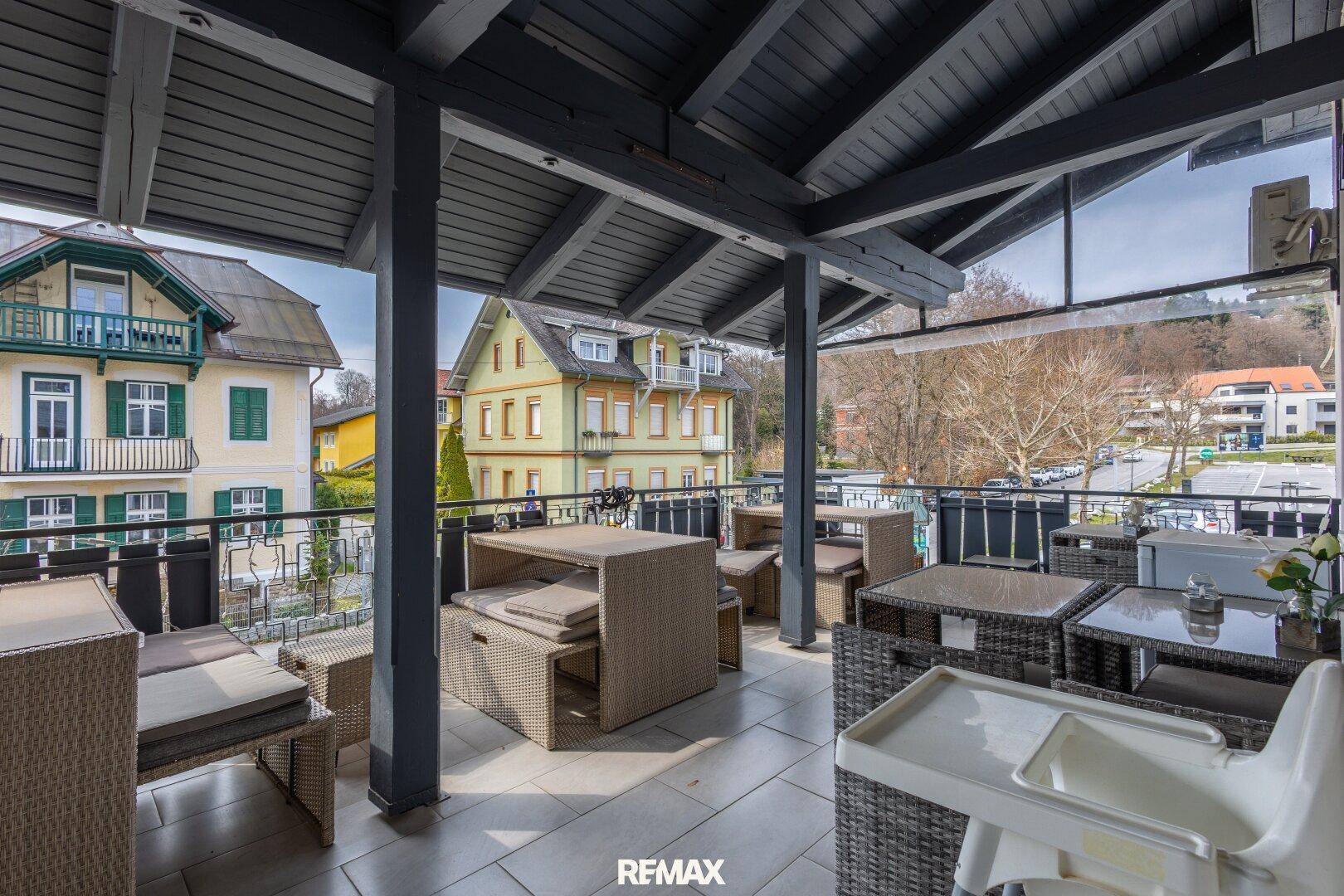 Überdachte Terrasse mit Sitzgelegenheiten und Blick auf die umliegenden Gebäude.