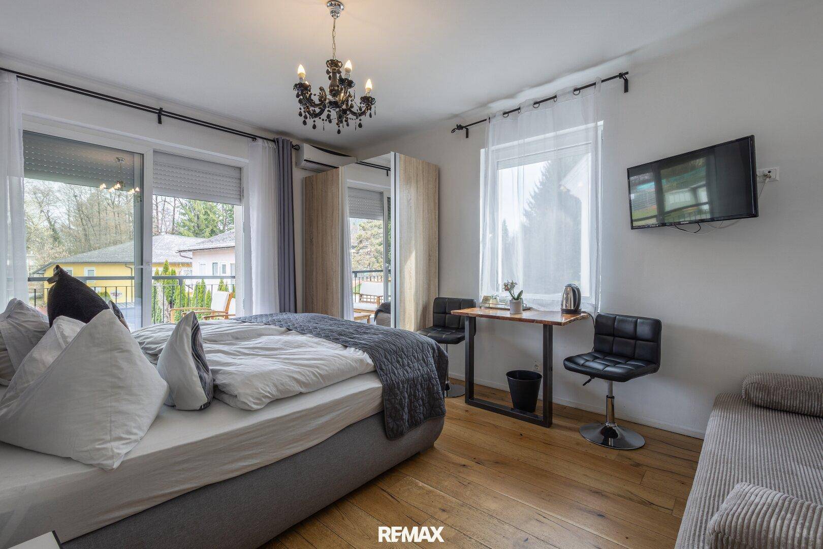 Helles Schlafzimmer mit Doppelbett, kleinem Tisch und Zugang zu einem Balkon.
