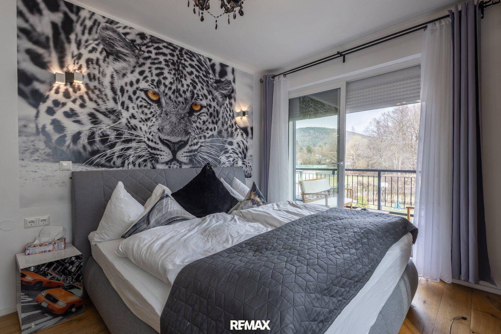 Geräumiges Schlafzimmer mit Leoparden-Wandbild und Balkonzugang mit Blick auf die Hügel.