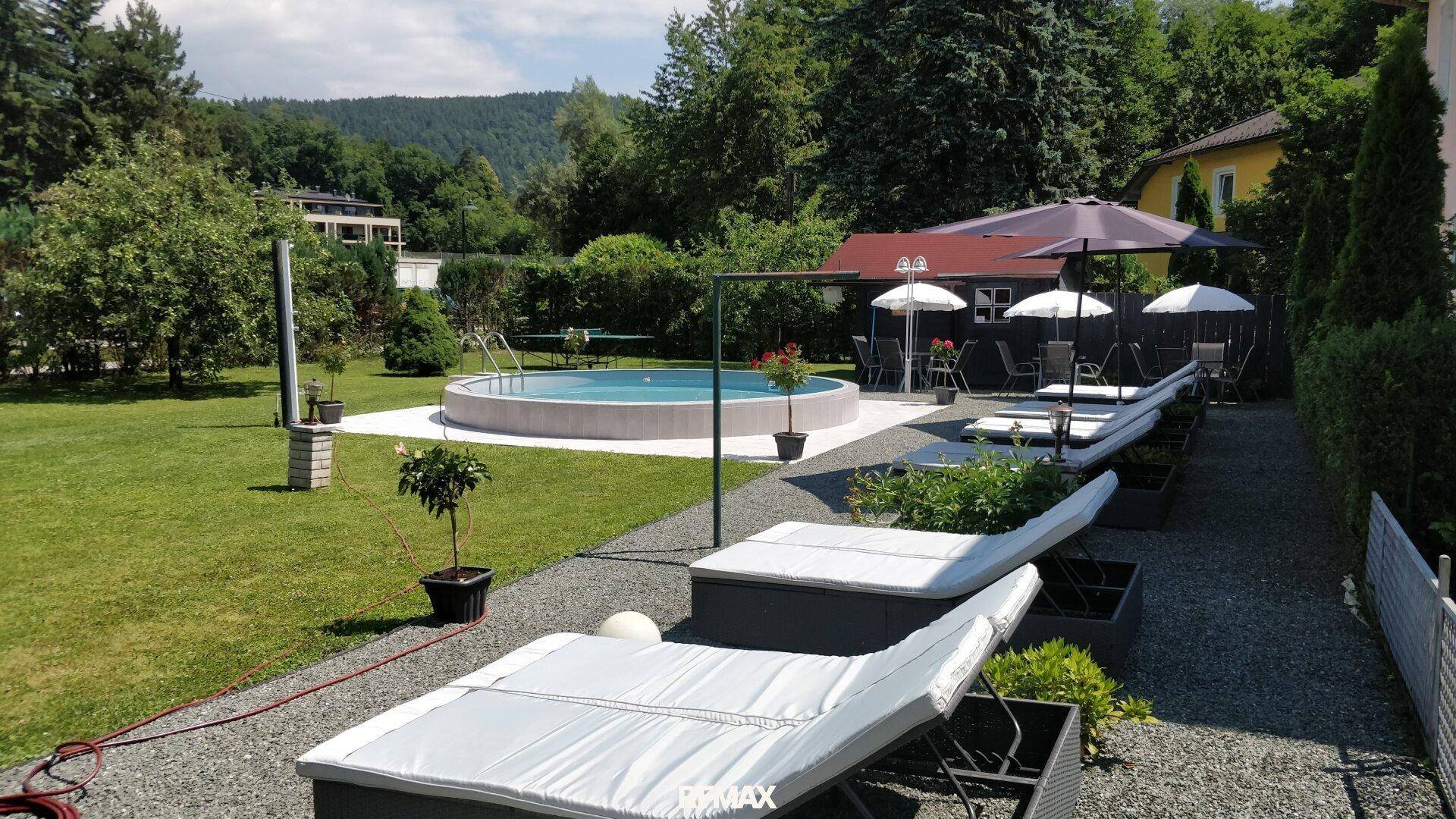 Gepflegter Gartenbereich mit Pool, Sonnenliegen und Sonnenschirmen für Entspannung.