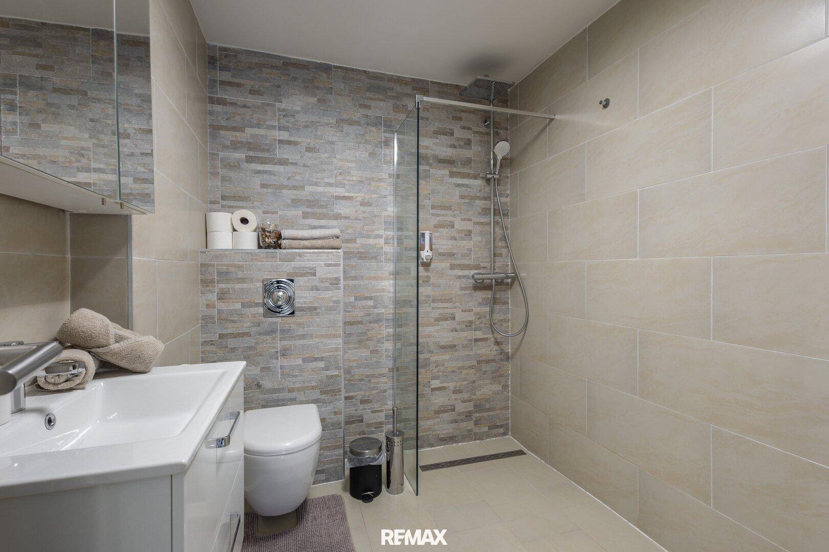 Modernes Badezimmer mit ebenerdiger Dusche, Hänge-WC und beigefarbenen Wand- und Bodenfliesen.