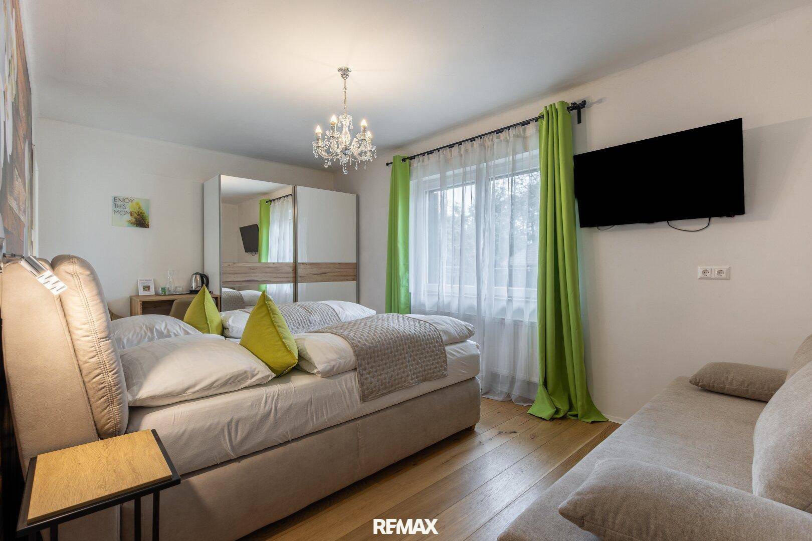 Schlafzimmer mit Doppelbett, Sofa, Holzboden und einem Kleiderschrank mit Spiegeltüren.