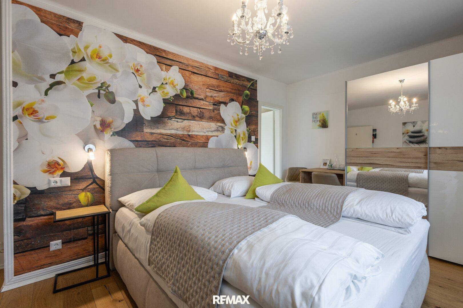 Gemütliches Schlafzimmer mit Doppelbett, floraler Wanddekoration und einem modernen Kleiderschrank.