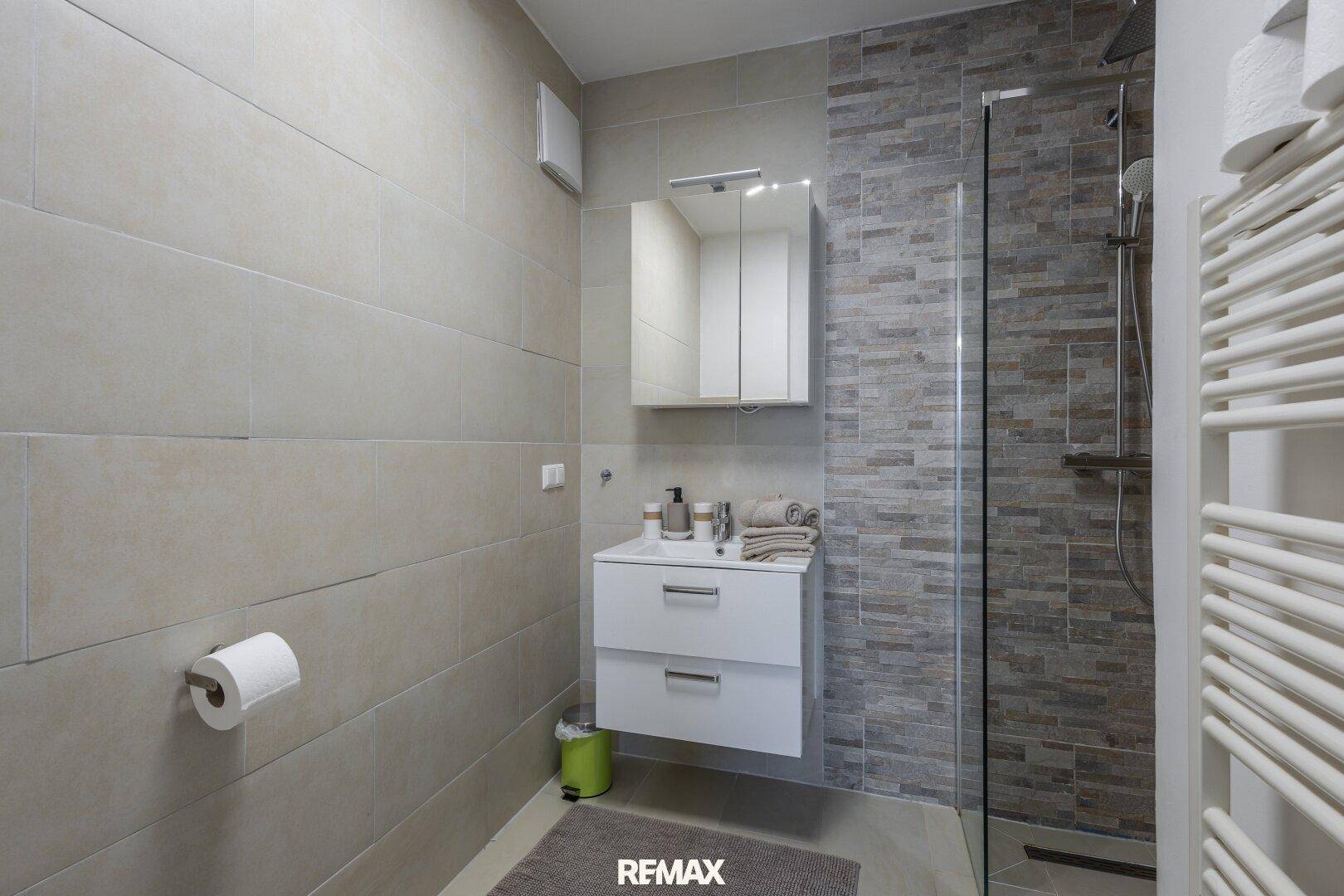 Modernes Badezimmer mit ebenerdiger Dusche, Waschbecken und beheiztem Handtuchhalter.