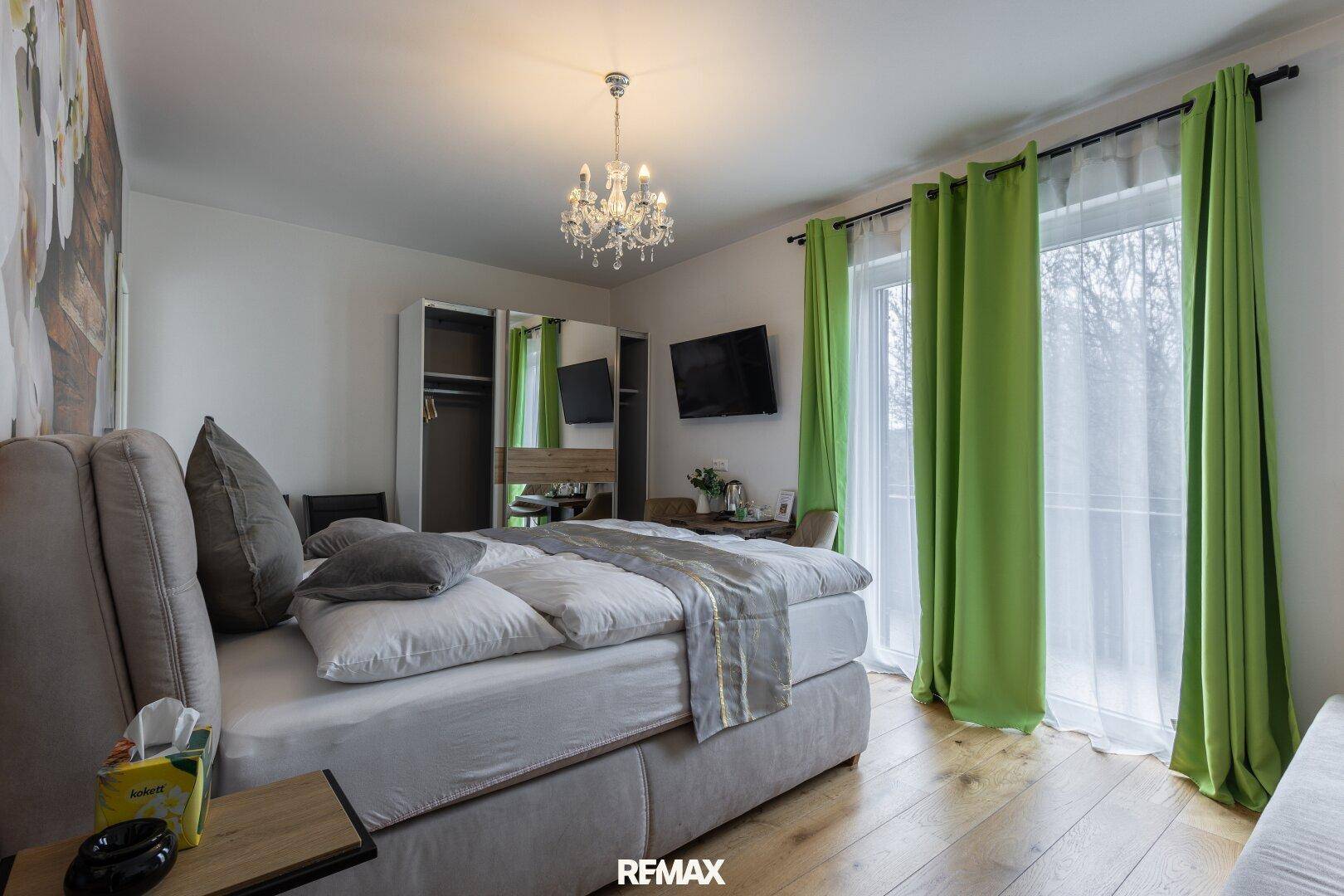 Schlafzimmer mit Doppelbett, Holzboden und Zugang zu einem Balkon durch eine Glastür.