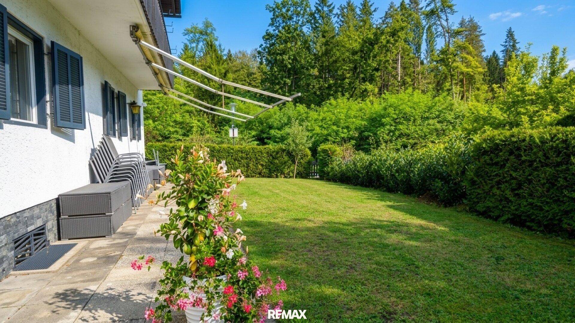 Gepflegter Rasenbereich hinter dem Haus, umgeben von hohen Hecken und Bäumen.