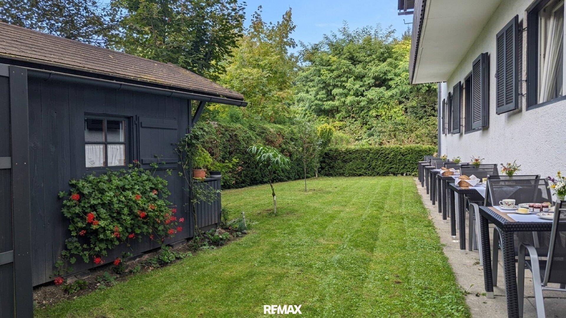 Gartenbereich mit Rasen, einem Gartenhaus und einer Reihe von Tischen und Stühlen.
