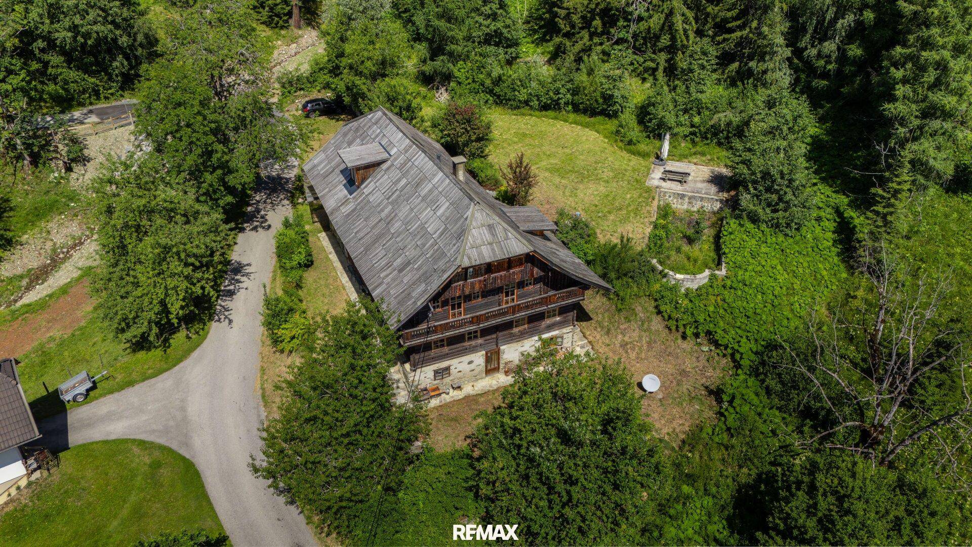 Luftaufnahme des traditionellen Holzhauses mit umliegendem Garten und Zufahrt.