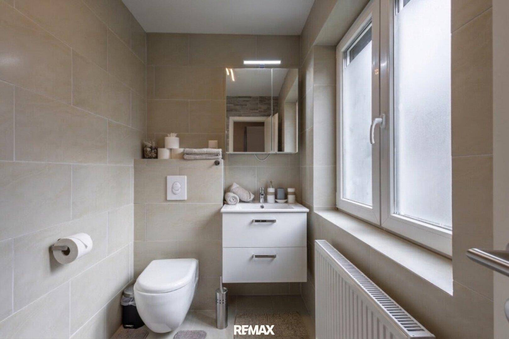 Kleines Badezimmer mit WC, Waschbecken und Fenster für Tageslicht.