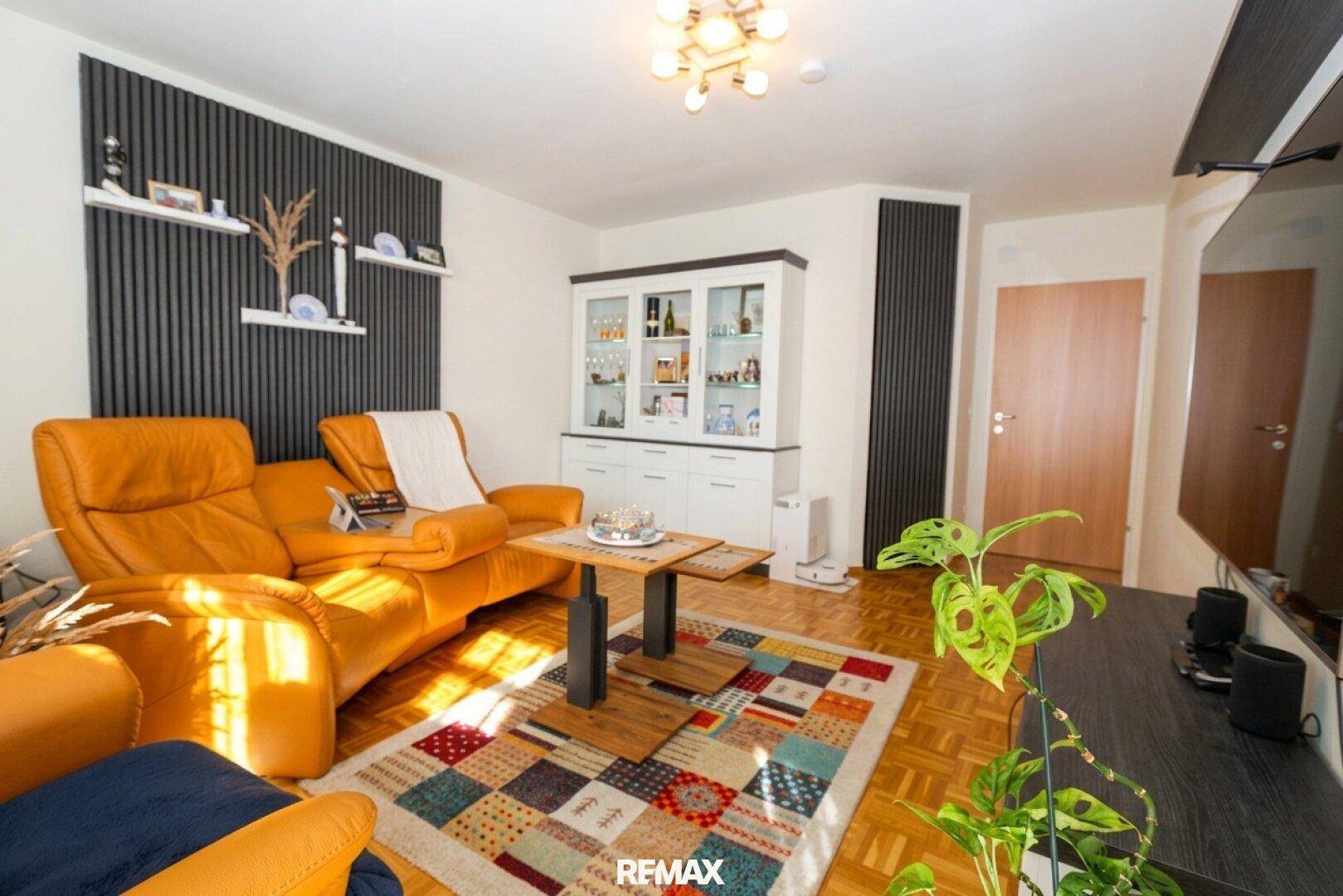 Gemütliches Wohnzimmer mit orangefarbenen Ledersofas, Parkettboden und dekorativer Wandverkleidung.