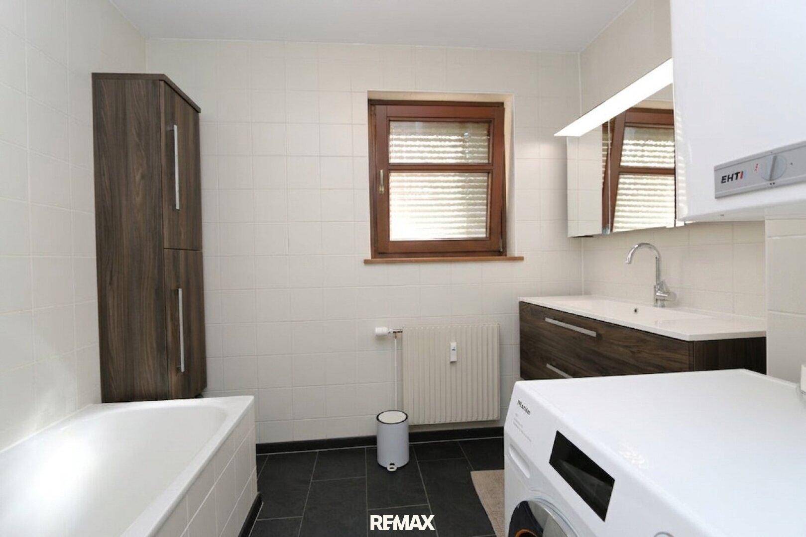Modernes Badezimmer mit Badewanne, Waschbecken, Waschmaschine und Fenster.