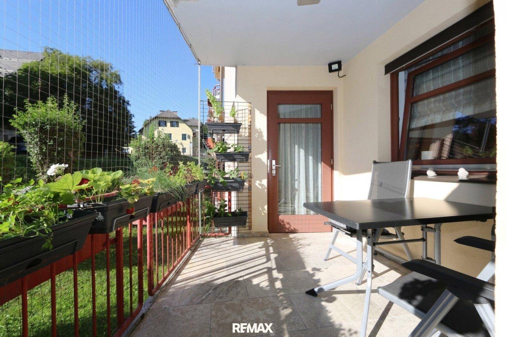 Sonniger Balkon mit Sitzgelegenheiten und Pflanzen, umgeben von einem Sicherheitsnetz.