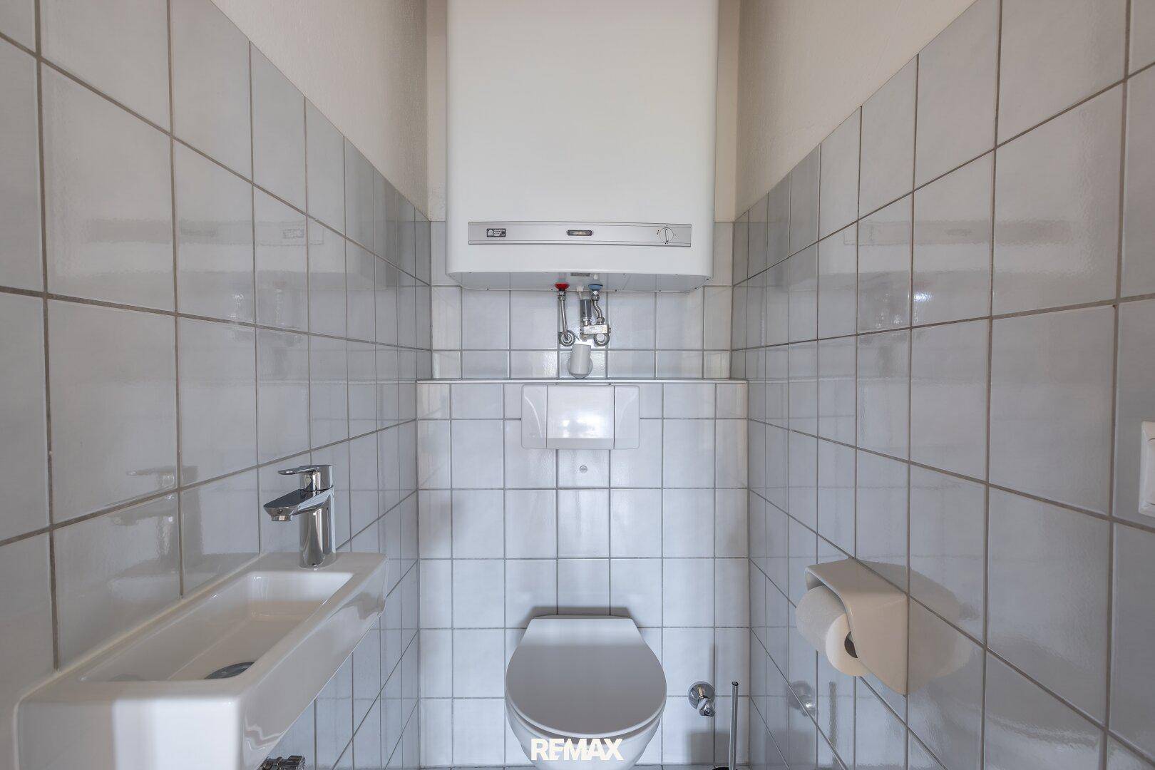Kleines Gäste-WC mit wandhängender Toilette, kleinem Waschbecken und hellen Fliesen.