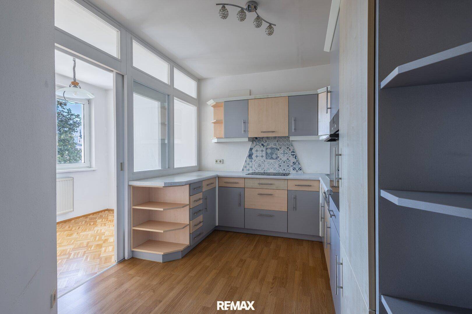 Helle Küche mit Holz- und Grautönen, integrierten Geräten und einem Durchgang zu einem weiteren Raum.