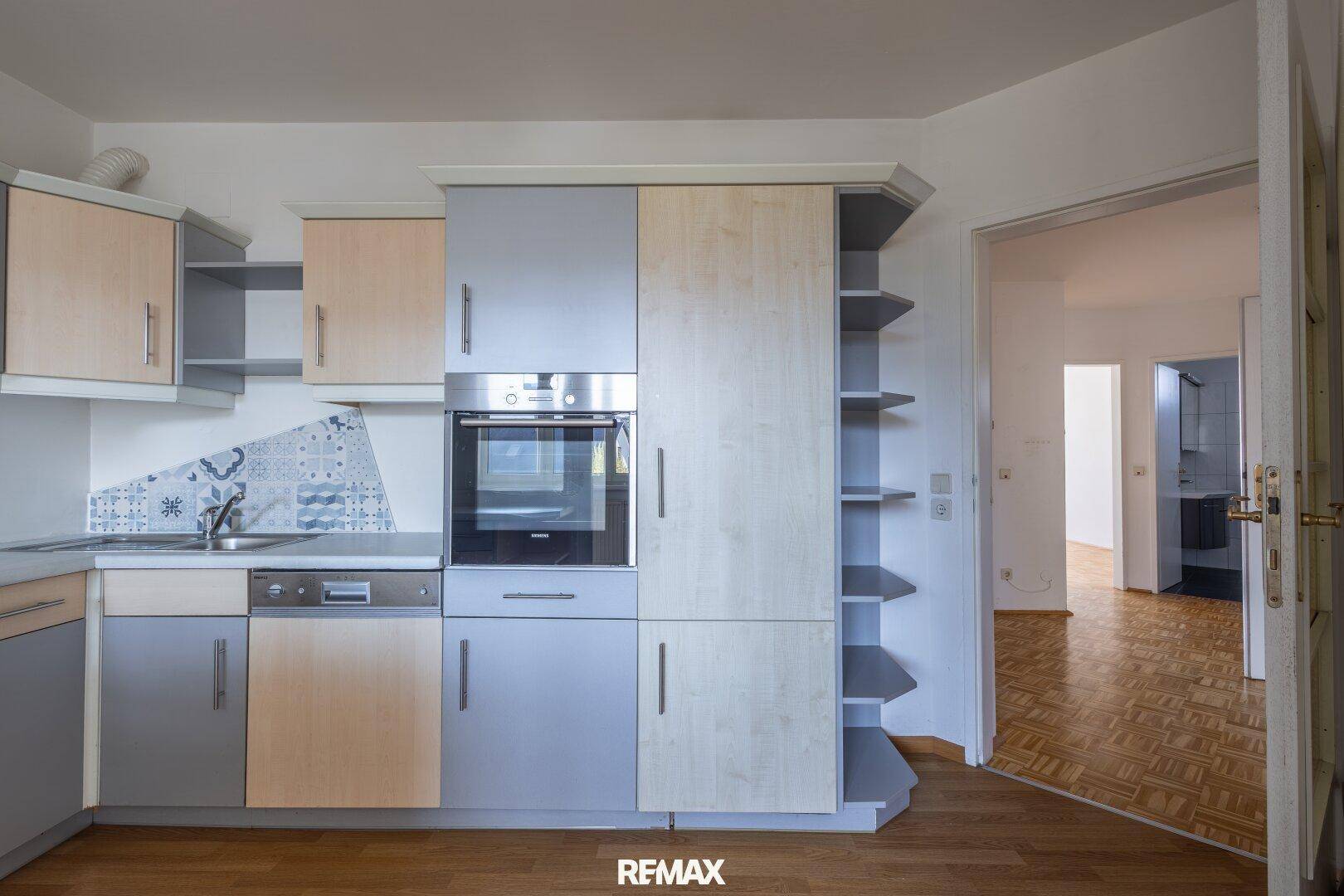 Funktionale Küche mit integriertem Backofen und Spülmaschine, die zu einem Flur führt.