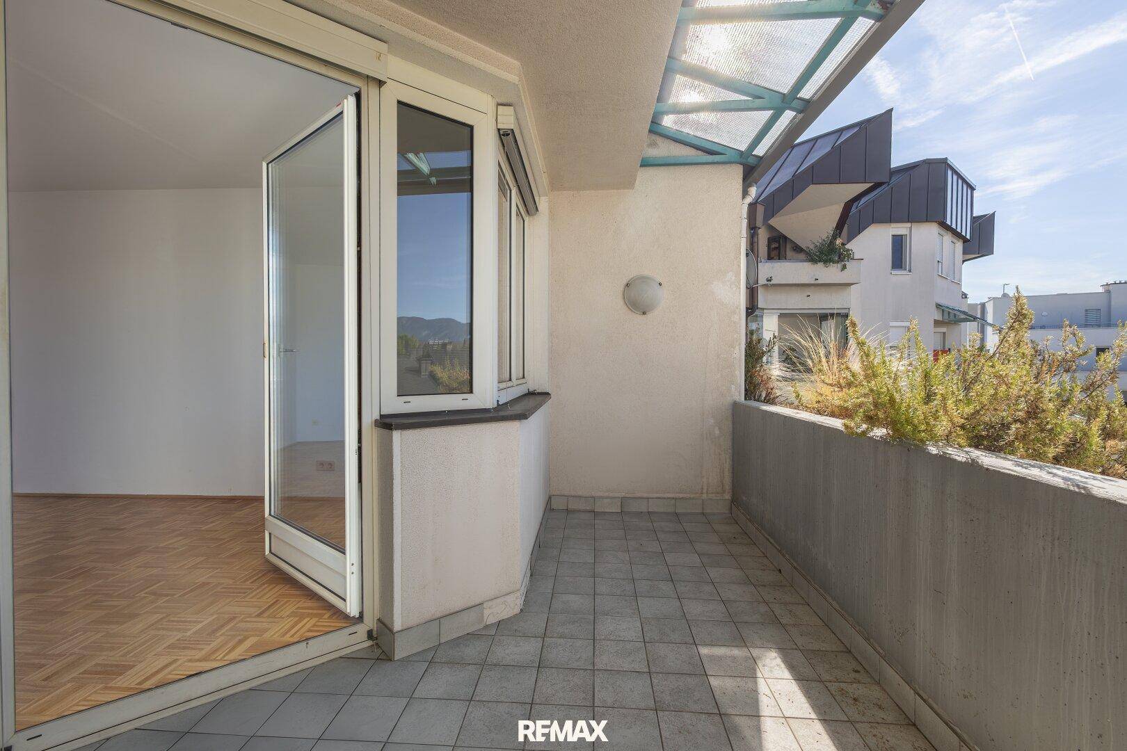 Geräumiger Balkon mit Fliesenboden und Blick auf die umliegenden Gebäude und Berge.