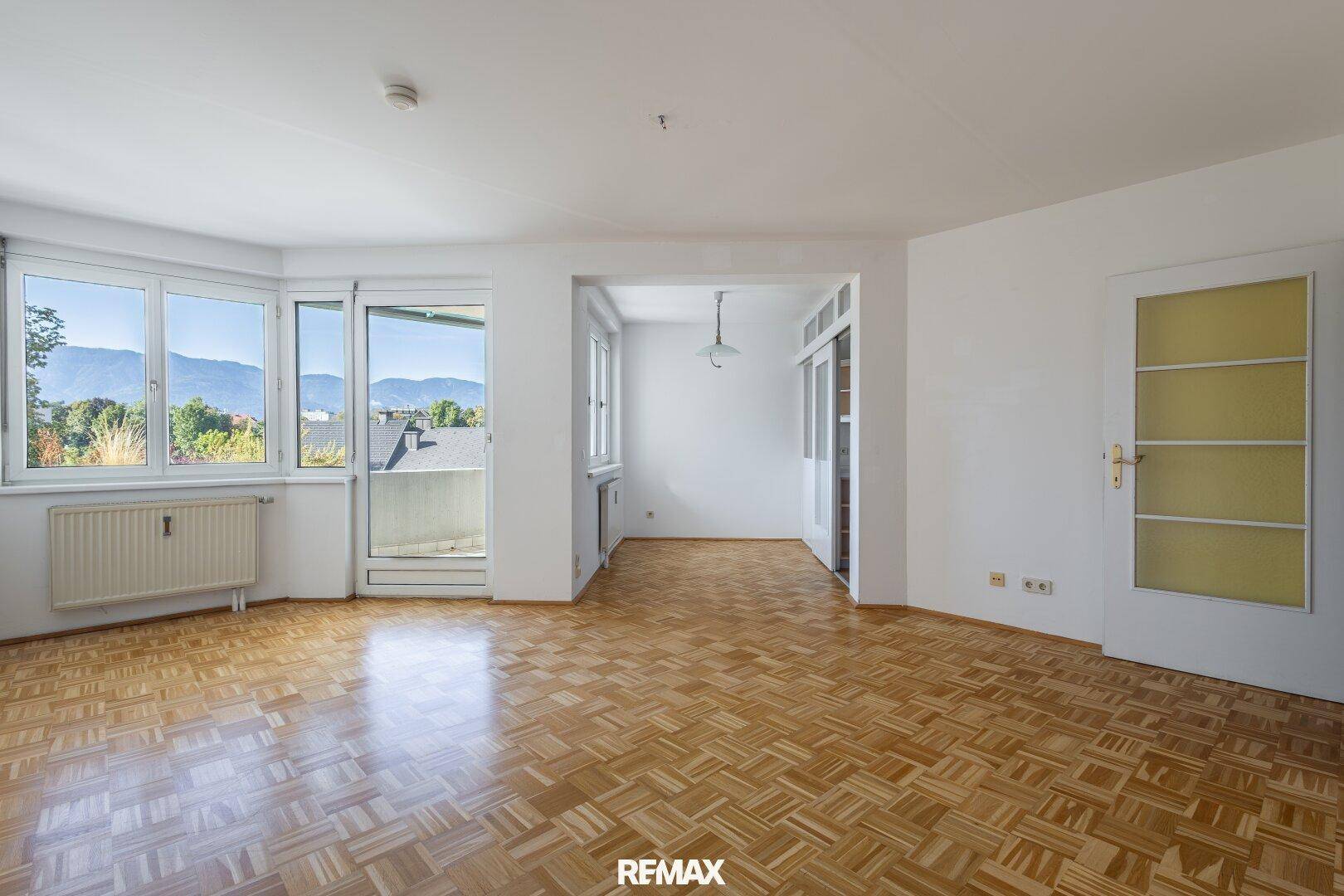 Geräumiger Wohnbereich mit Parkettboden und Zugang zu einem Balkon, ideal für einen Essbereich.