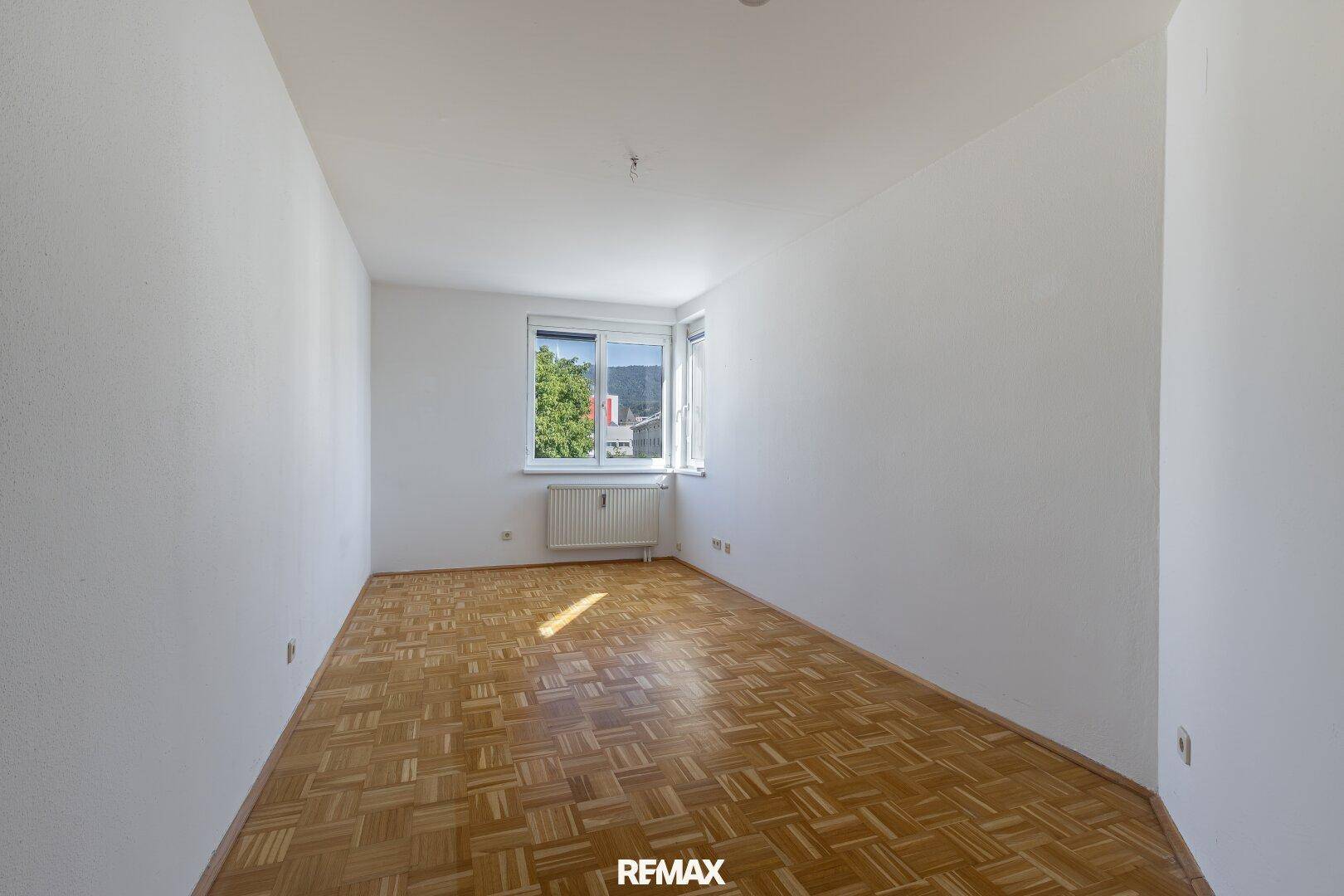 Leeres Schlafzimmer mit Parkettboden und Fenster, das einen Blick auf die Berge bietet.