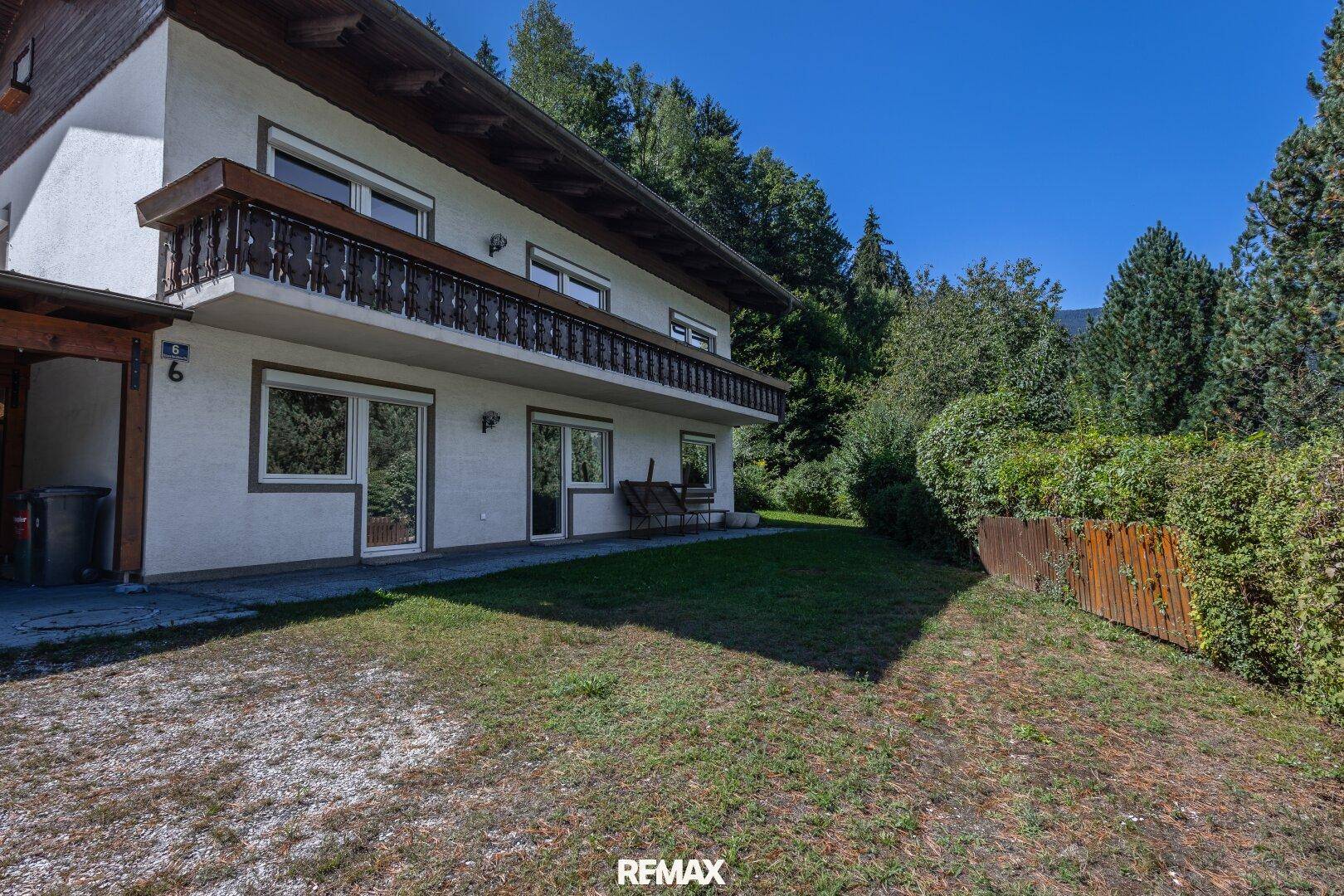 Seitenansicht des Hauses mit gepflegtem Rasen und üppiger grüner Bepflanzung im Hintergrund.