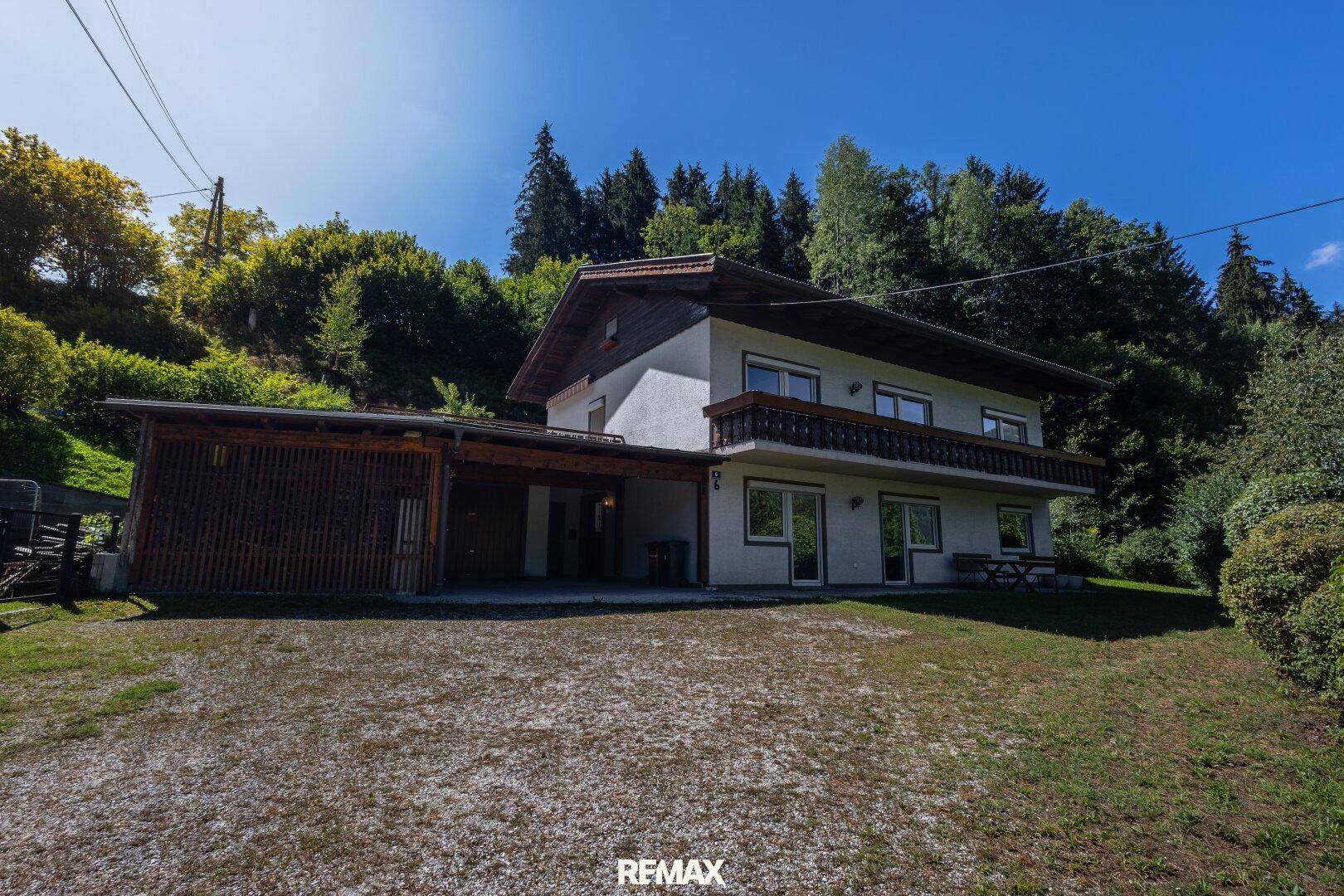 Vorderansicht des Hauses mit Carport, großem Vorplatz und umgebendem grünen Rasen.