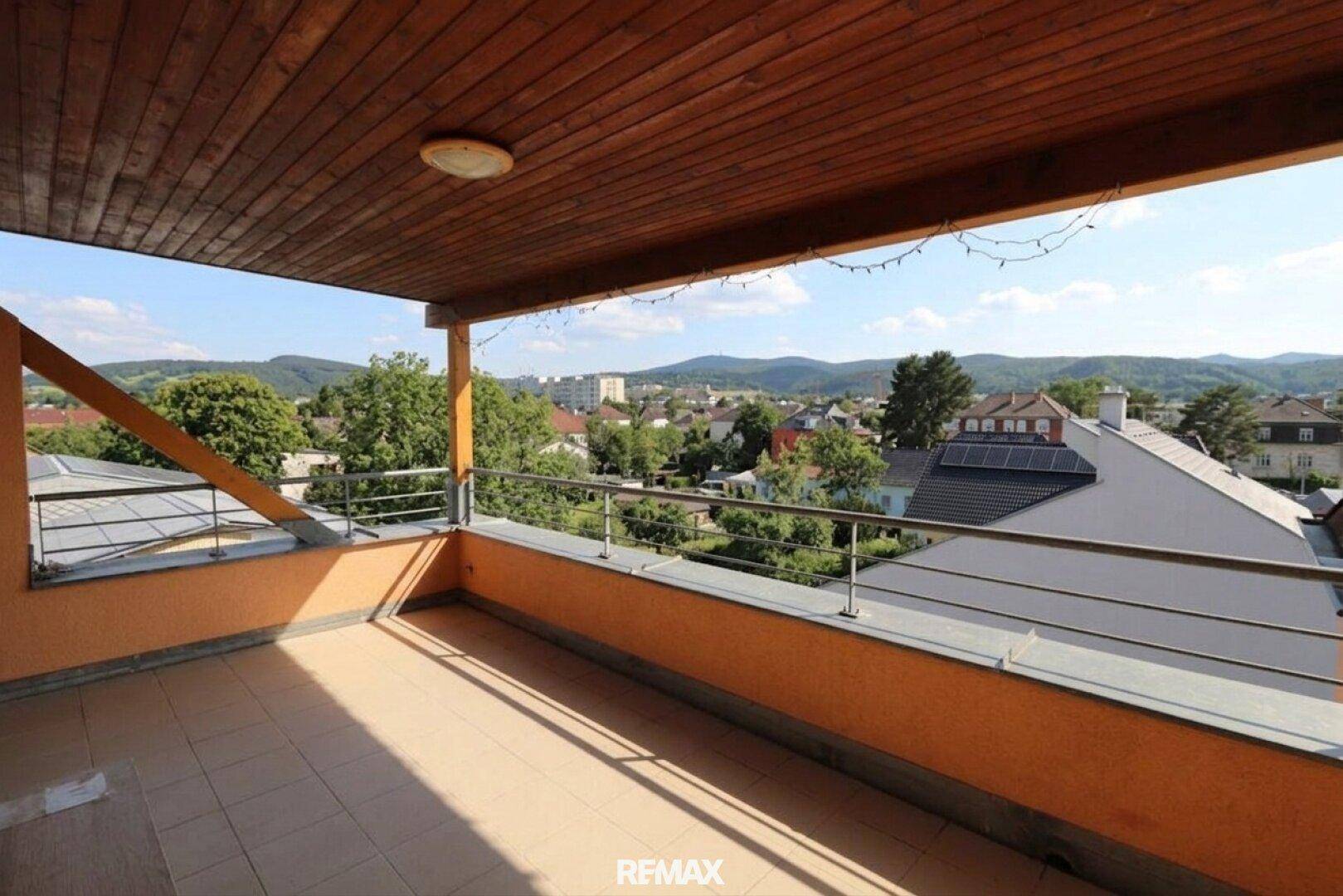 Große Dachterrasse mit Holzdecke und Metallgeländer, bietet eine weite Aussicht auf die grüne Umgebung.