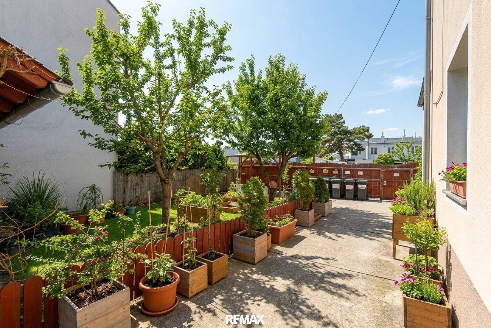 Gepflegter Gartenbereich mit Bäumen, Pflanzen in Töpfen und einem kleinen Zaun, ideal zum Entspannen.